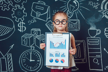 The little smart girl in glasses shows graphics company's business activity on a background of wall with picture