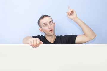 Surprised young man portrait. Finger pointing up. Advertising te