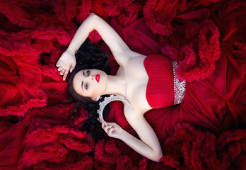 beautiful brunette in a crown with a bouquet in his hand and in a chic big and lush red dress in the park among the green