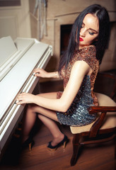 Obraz na płótnie Canvas Beautiful brunette girl in a brilliant dress in the restaurant plays piano