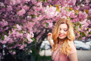 Fototapeta premium Young beautiful blonde girl with long hair in a pink dress near the cherry trees
