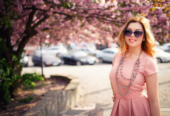 Young beautiful blonde girl with long hair in a pink dress near the cherry trees