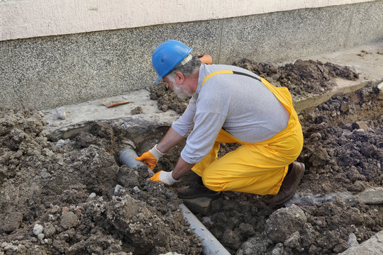 Plumber at construction site installing sewerage tube