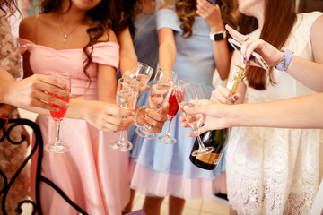 Hands of young girls decorated with manicure holding glasses filled with champagne at a party