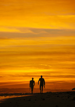 Surfing couple walking at sunset, Rincon, Santa Barbara, California, United States of America