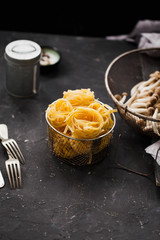 Raw tagliatelle pasta in plate over dark table.