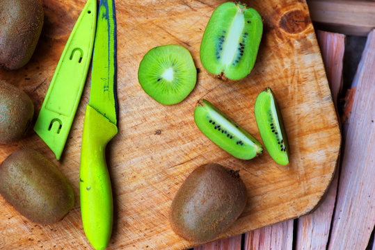 Fresh sliced kiwi fruit and knife on wooden board, top view