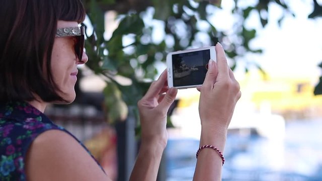 Young woman shoots video on smartphone, yachts and ocean. Close-up. Young sexy woman with glasses using smartphone in her journey to Bali island, Indonesia.