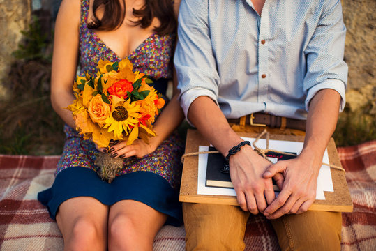 Man with sketchbook and woman with a bouquet of flowers sitting on a plaid