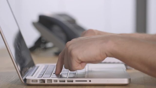 Male hands finger typing on silver laptop, defocussed modern office background