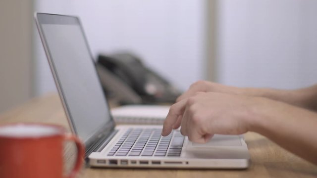 A man finger typing fast on a silver laptop, modern office background