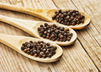 Black pepper in wooden spoon on the old board