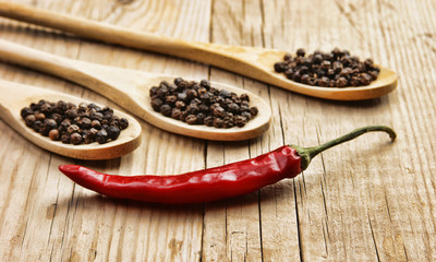 Black and red pepper in wooden spoon on the old board