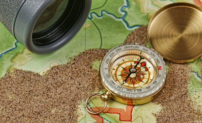 Fototapeta na wymiar binoculars and a compass on the map with sand