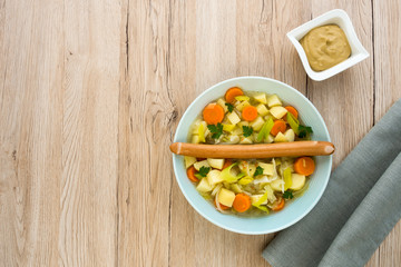 
Sausage stew with one large Frankfurter sausage on top of chopped carrots, leak and potatoes. View from directly above and lots of copy space. 