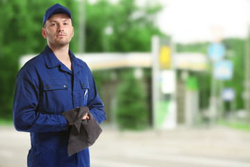 Young mechanic in uniform with rag standing on blurred petrol station