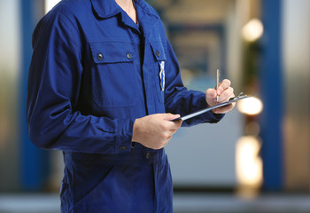 Mechanic in uniform with a clipboard and pen on gas station blurred background - obrazy, fototapety, plakaty