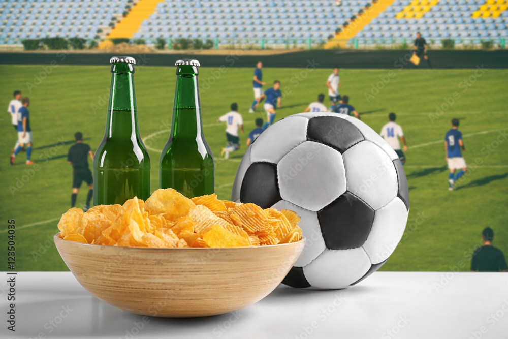 Wall mural Beer with snacks and football ball on green field background