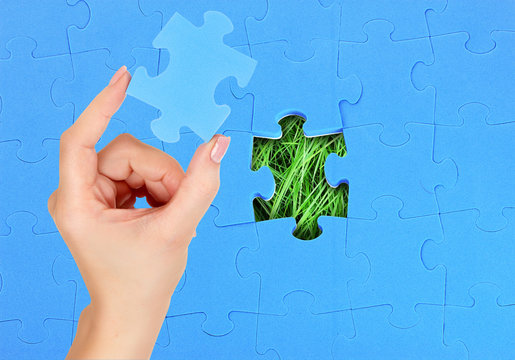 Female hand with missing puzzle piece. Blue pazzle over green grass background.