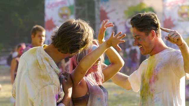 Cheerful young men and woman having fun at concert, friends colored with powder