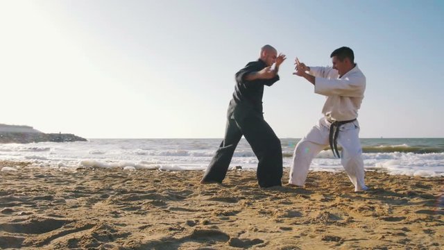 two professional karate fighters on the beach sea background, slow motion