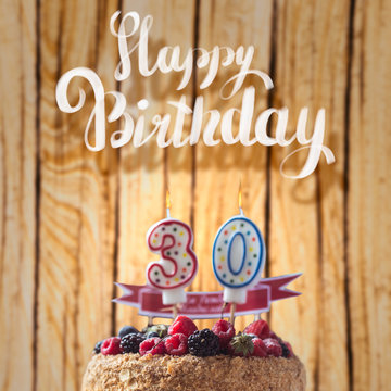 raspberries blackberry cake with candles number 30 on wood background and Happy Birthday lettering