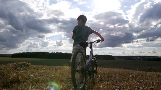 Boy with bike standing in a field at the top and looking, than going