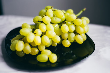 A branch of green grapes is  lying on a black plate. Background