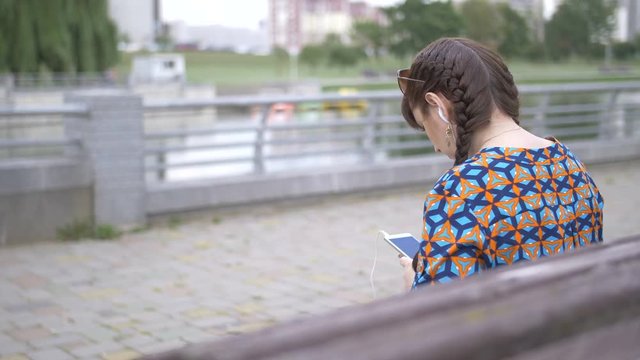 young woman sitting on a bench in the park and listening to music from your phone
