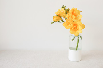 Yellow Freesia flowers in vase on white linen table