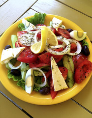 Greek salad in a yellow plate on a wooden table