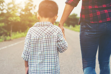 Mother holding a hand of his son in summer day walking on the st