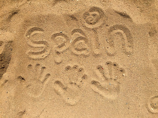 Three hand prints in the sand in Spain with the word Spain written in the sand.