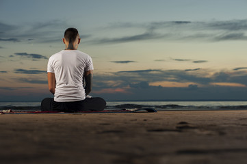 Fototapeta na wymiar Tattoo man meditating on the beach at sunset
