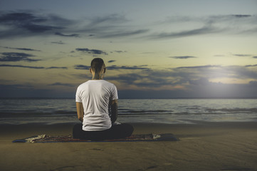 Young tattoo man practicing yoga at sunset