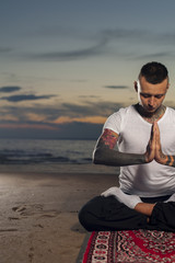 Tattoo yoga man meditating on the beach at sunset