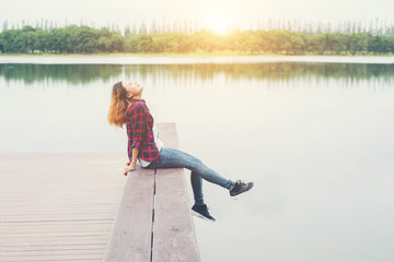 Fototapeta na wymiar Young hipster woman sitting on wooden pier, Relaxing lying leg d