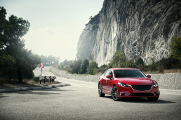 Red car standing on the road near mountains at daytime - obrazy, fototapety, plakaty