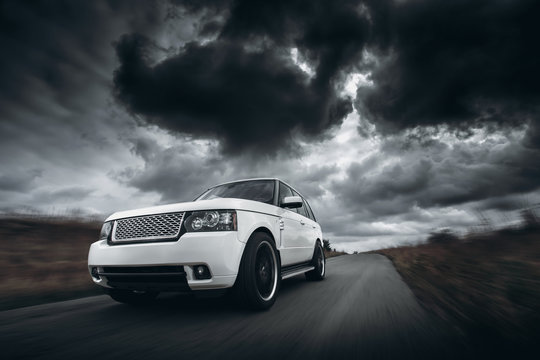 Fototapeta White car speed driving on road at dramatic clouds daytime