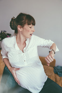 Expectant mother timing her contractions while sitting on couch at home