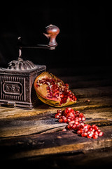 Old coffee grinder and pomegranate seeds scattered on old wooden table. Painted with light 