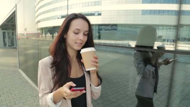 Pretty girl walking and using app on smartphone drinking coffee. Steadicam shot.