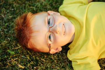 Happy baby boy with red hair in glasses on grass