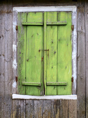 Old wooden house window closed with green colored shutters    