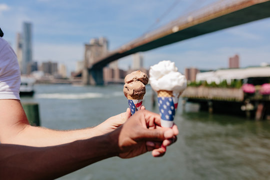 Gay Couple Holding an Ice Cream with an American Flag in front of The Brooklyn Bridge . NYC