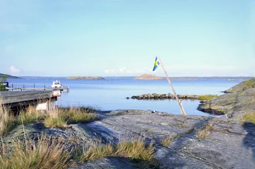Fototapeten Sommardag på västkusten. En gammal svensk flagga svajar i luften ovanför klipporna.  © glimpseofsweden