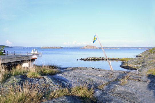 Sommardag på västkusten. En gammal svensk flagga svajar i luften ovanför klipporna. 
