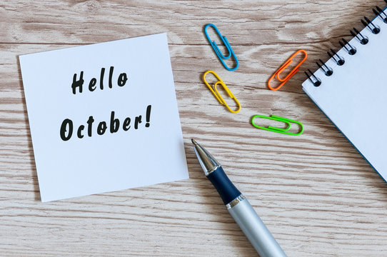 Paper with words HELLO OCTOBER and office suplies lying on wooden table, home or job workplace. Autumn concept