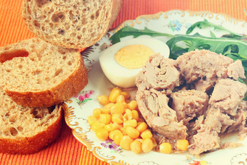 Canned tuna, sweet corn, boiled egg, sliced rye bread with bran and fresh salad leaves (rucola) on a bright color napkin. Mediterranean food. Toned colors style photo