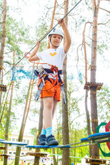 Young girl in harness climbing and trying facilities in an adventure park.